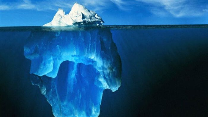 Et fritt flytende isberg i et åpent, mørkt hav, der isbergets massivitet er skjult under vannets overflate.