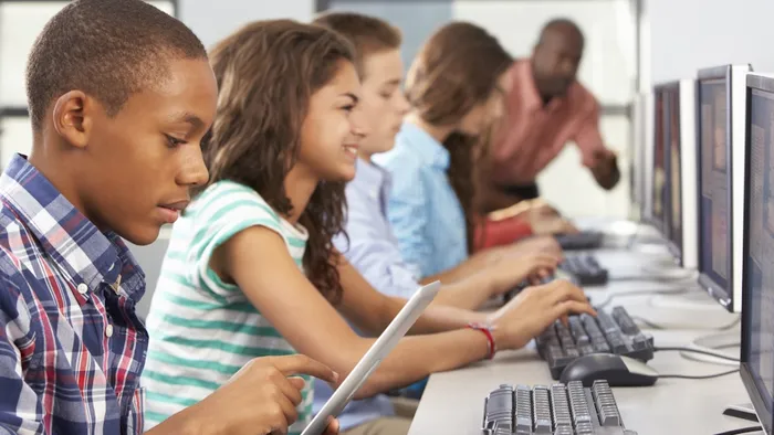 bilde av elever som jobber på pc og lærer går rundt og hjelper