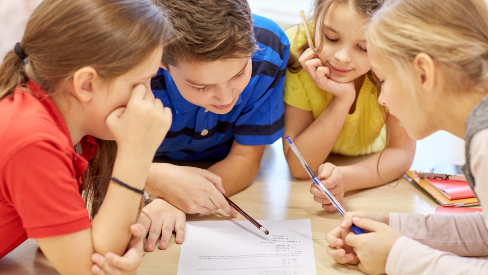 Fire barneskoleelever samarbeider om en oppgave med blyant og papir.