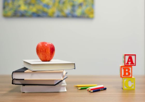 Illustrasjonsbilde fra et klasserom av bøker, fargeblyanter og et eple