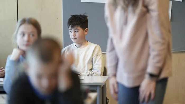 Klasserom, barn som sitter, lærer i bakgunn, fokus på barn bakerst i klasserommet