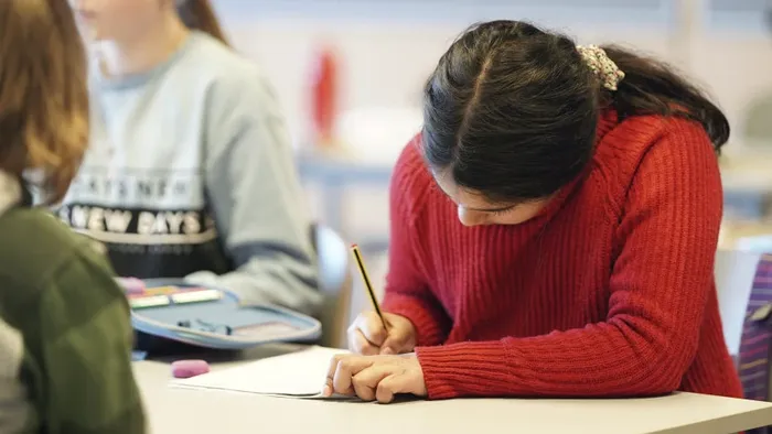 Ei jente med rød genser sitter i et klasserom, skriver i en bok
