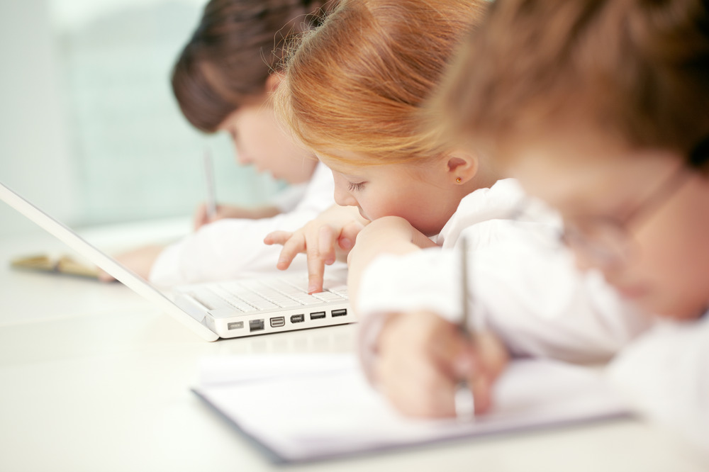 a girl and a boy writing. Another girl is on the laptop.
