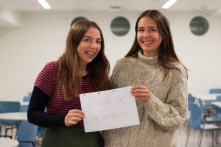 Foto av to studenter som holder en plakat der det står "Praksis er samarbeid"