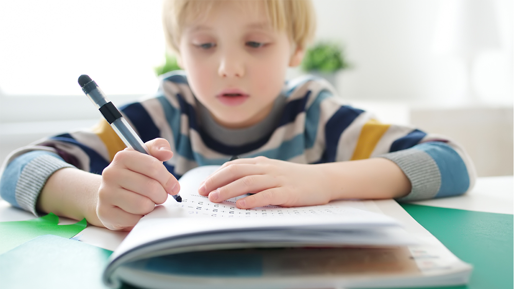 Illustrasjonsfoto tett på en ung gutt som konsentrerer seg om regnestykker.