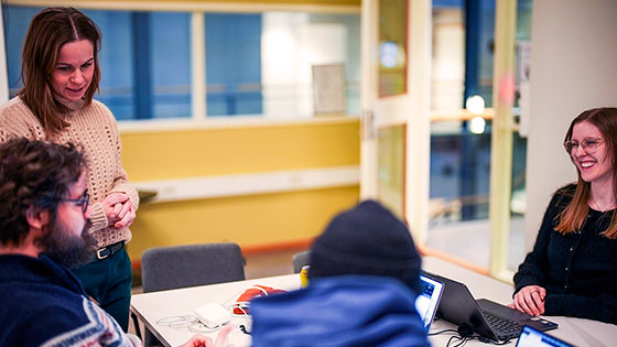 Fire mennesker i et gult møterom på univeristetet i Oslo. De jobber i gruppe hvor to personer skriver noe på en laptop.