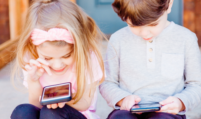 Gutt og jente i 5-årsalderen sitter med hver sin smarttelefon og ser på skjermen.