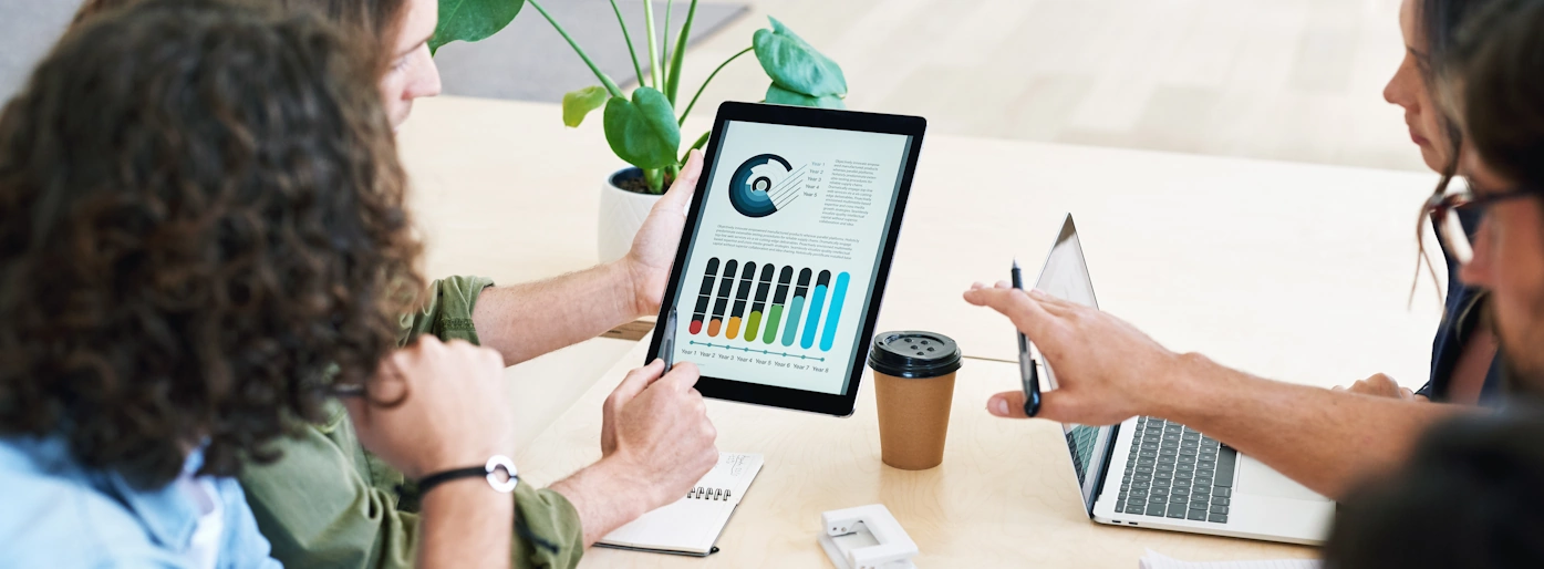 Three women and a man collaborating in front of a tablet with statistics on it.