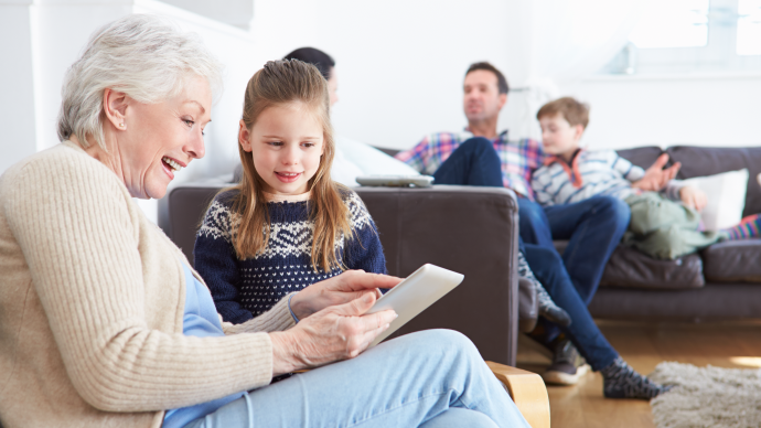 Elderly woman and eight year old girl looking at a tablet together. Illustration photo.