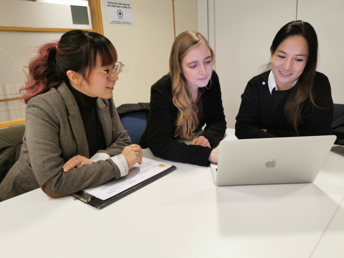 Tre kvinnelige studenter samarbeider ved et bord, foran en pc-skjerm