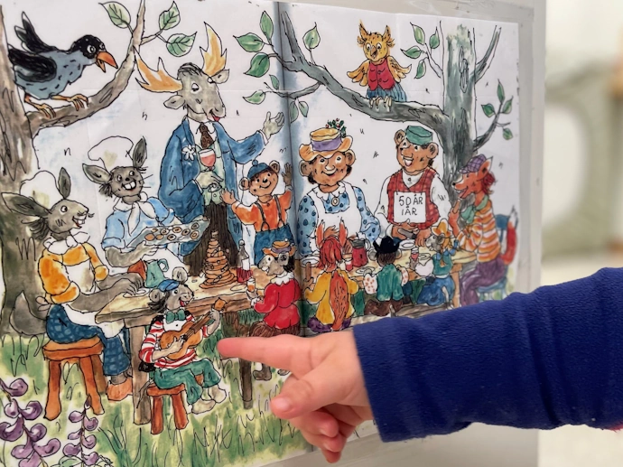 A children's hand pointing to a picture from Thorbjørn Egner's story Huckybucky Forest.en