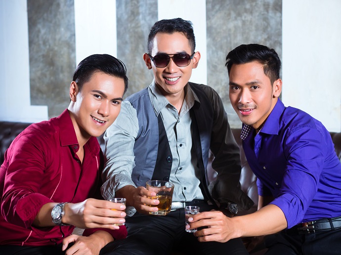 Tre menn av asiatisk opprinnelse med hver sin drink som skåler og smiler mot kamera. Foto