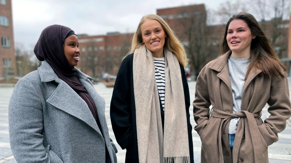 Tre kvinnelige studenter står på plassen utenfor Helga Engs hus på Blindern, UiO.