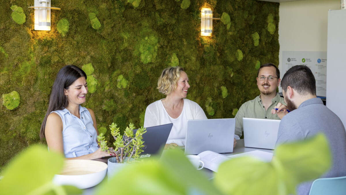 Fire ansatte ved Institutt for pedagogikk sitter i et møte på et kontor med en vegg laget av mose.