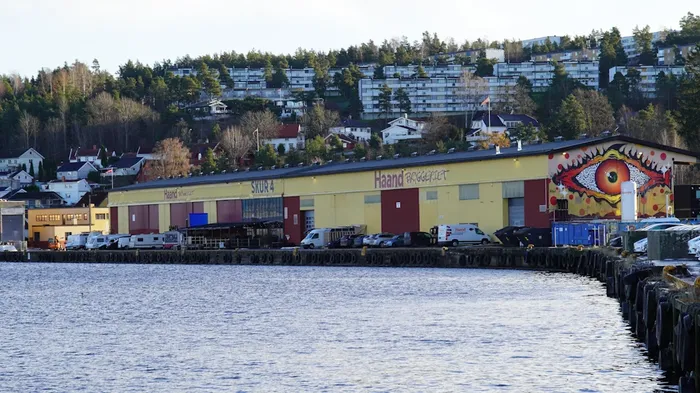 Ei kai med biler på og vann i forgrunnen av bildet. Bymiljø med boliger og blokker i bakgrunnen. Tangenkaia i Drammen.