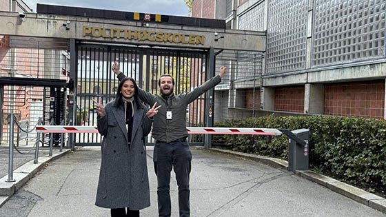 En mann og en dame utenfor politihøyskolen. De holde armene i været og ser veldig fornøyde ut.