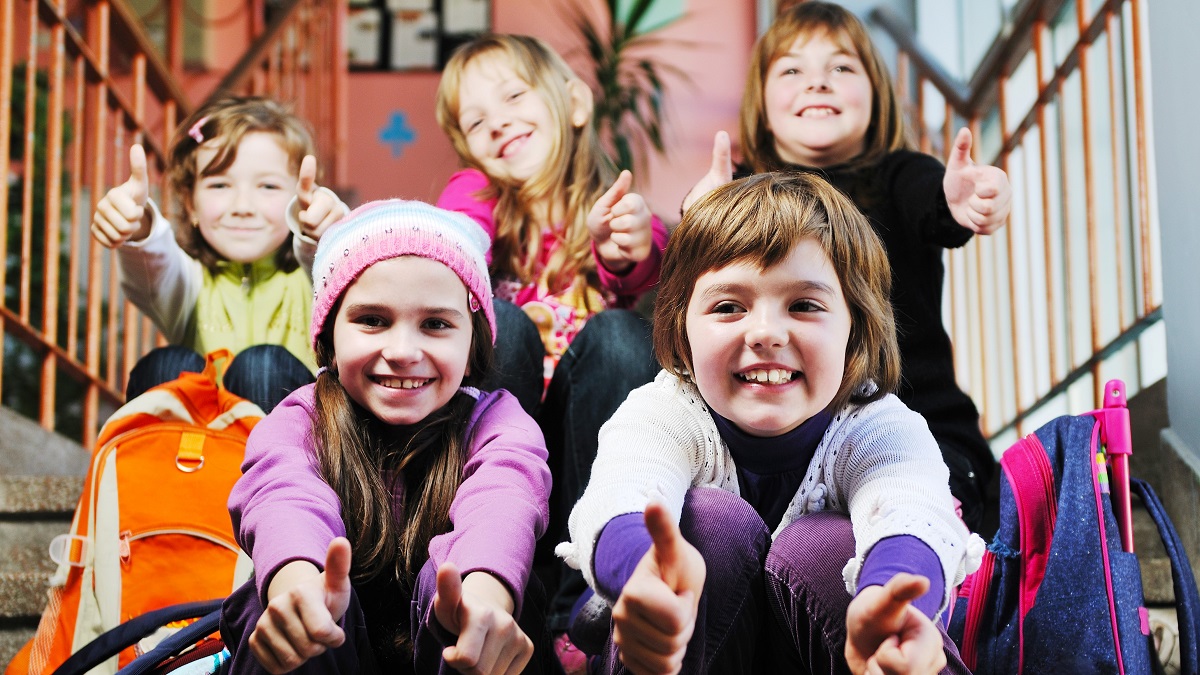 fem barn som sitter i skoletrappen og viser glede og tommel opp
