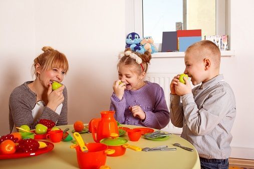 barn som leker at de de spiser, med voksne i barnehagen. Foto.