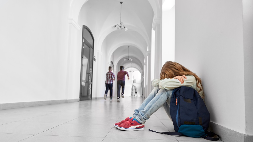Jente sitter alene med hodet i fanget i skolekorridor.