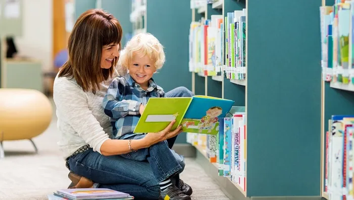 bilde av barn som ser i bok sammen med voksen ved en bokhylle