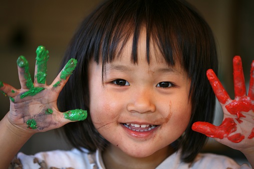 Asiatisk jente som viser sine hender med maling. Foto.