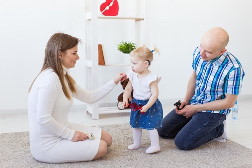 mor og far sitter på gulvet og snakker med barn med høreapparat