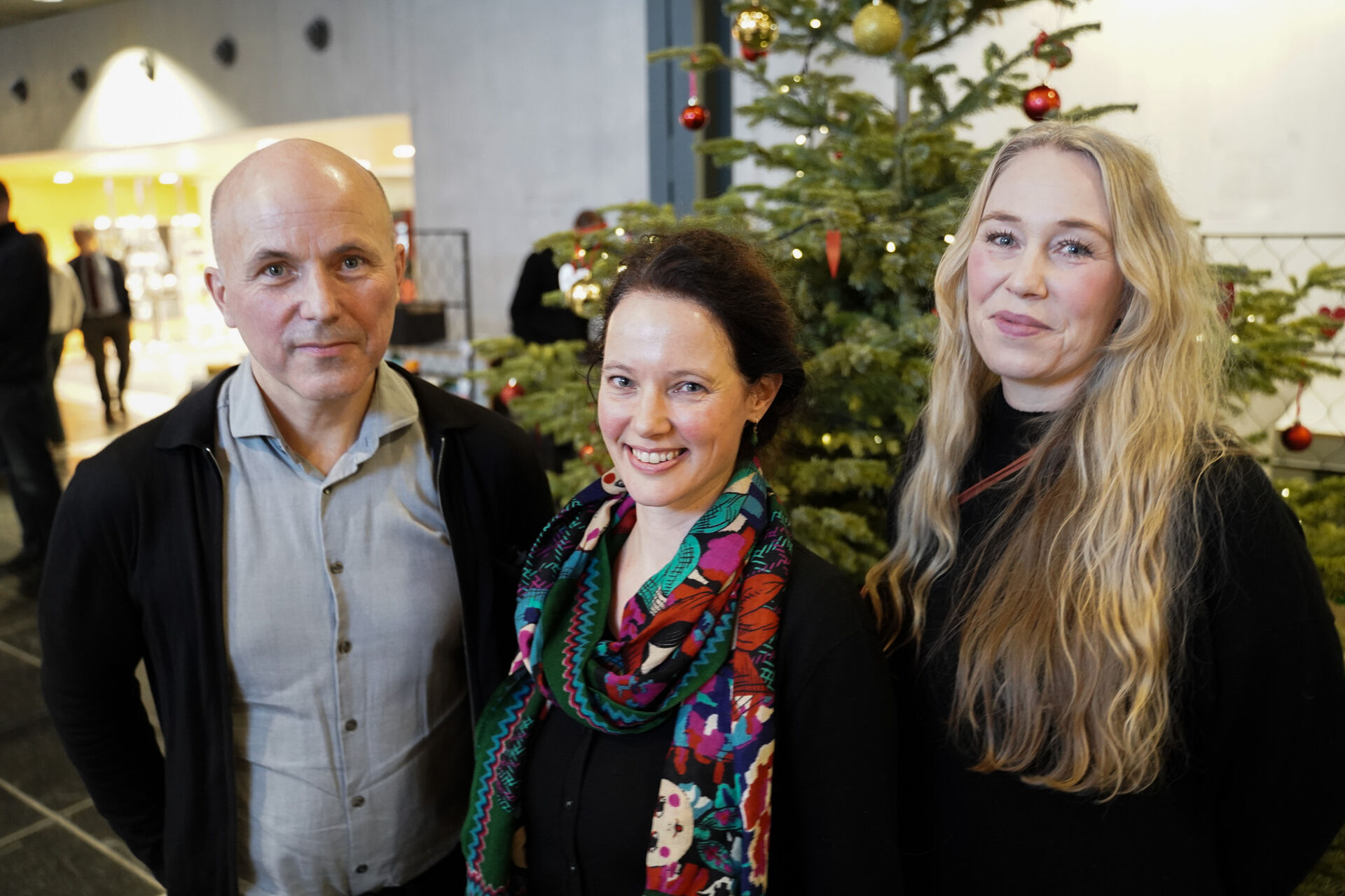 De tre prisvinnerne står foran et juletre og smiler