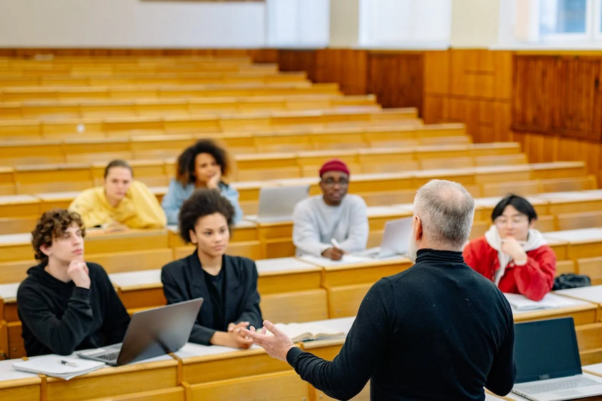 A teacher is speaking to small group of students in a lecture hall.