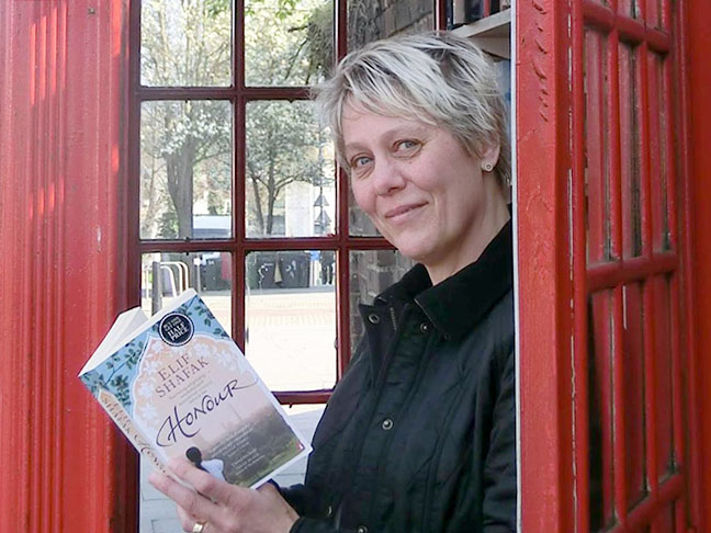 Anna Nissen standing in a phone box library reading a book