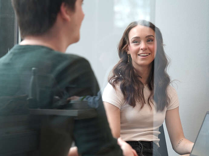 En kvinnelig student som er vendt mot kamerat smiler mens hun snakker med en mannlig i forgrunnen
